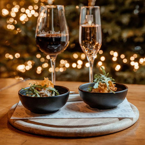 Houten plankje met daarop twee bakjes met amuses met daarachter een glas rode wijn en een glas bubbels en kerstversiering